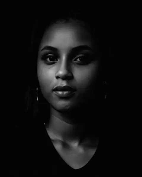 Black-and-white portrait of Chioma Peace, lit softly from one side against a black background, looking directly at the camera.