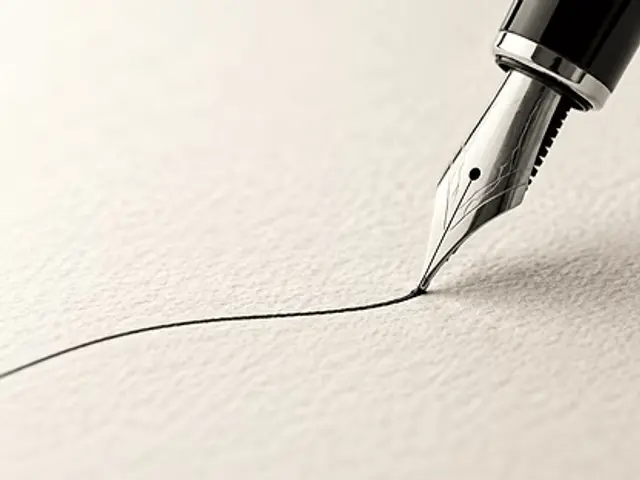 A silver fountain pen nib drawing a thin line of black ink across textured off-white paper.